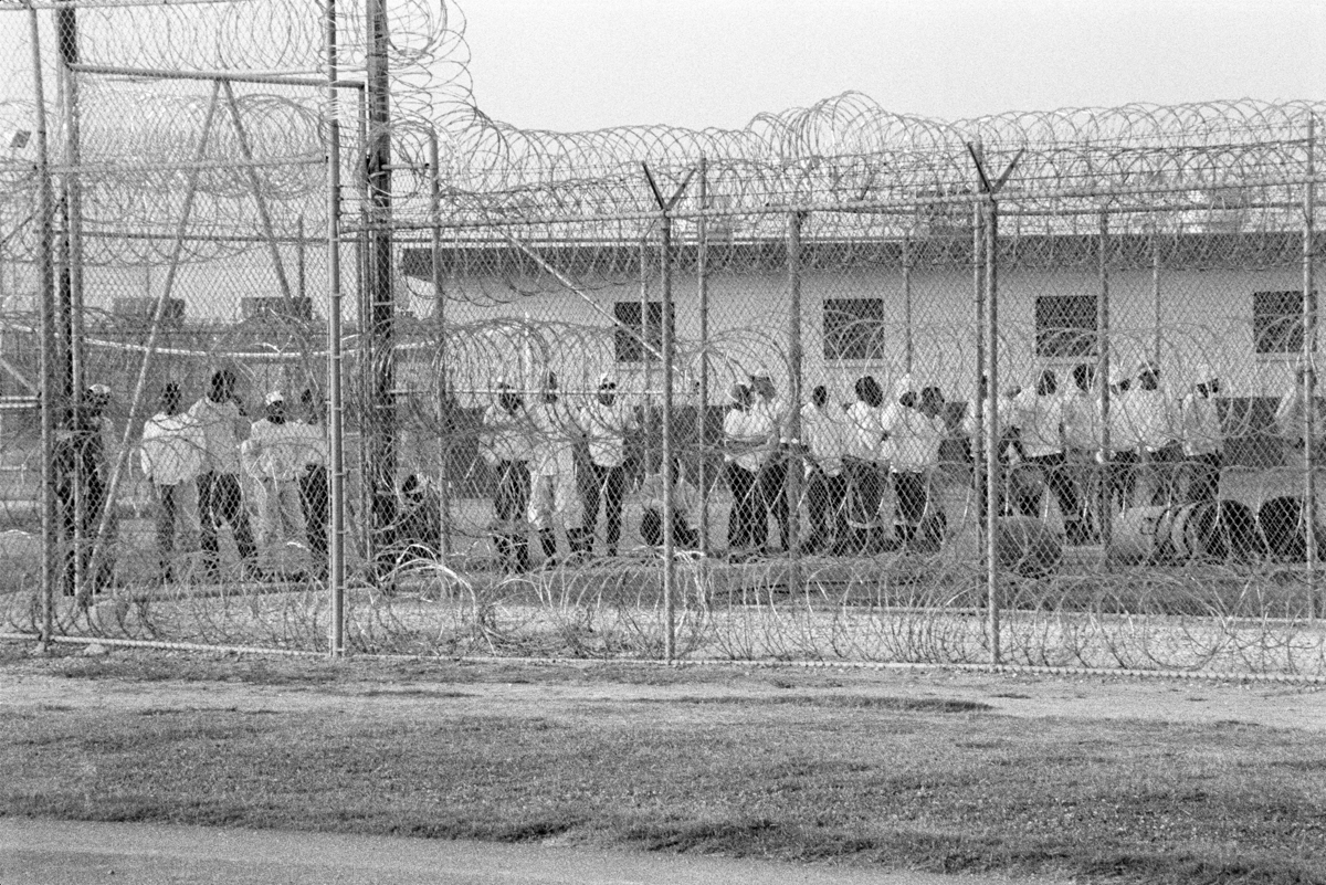 Chandra McCormick, Work Call, Hombres detrás de cercas de alambre de púas esperando para ir a trabajar en los campos de Angola., 2004. Impresión de pigmento de archivo. Cortesía del artista.